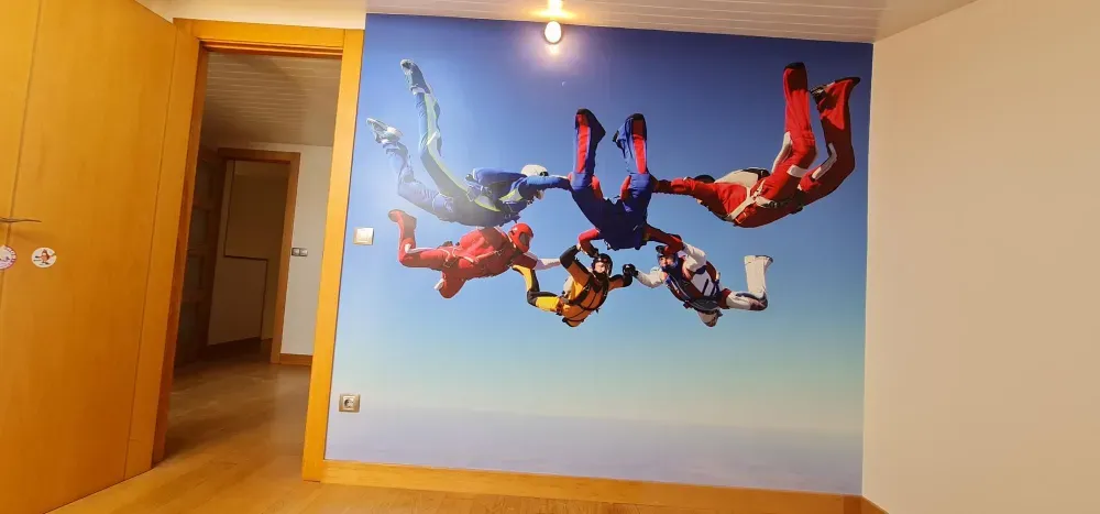 Paracaidistas con trajes coloridos contra un cielo azul, en un mural de pared en una habitación con una puerta