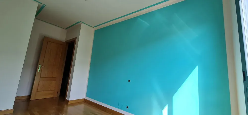 Una habitación con paredes azules, puerta de madera y suelo de madera. La luz entra a raudales por la ventana.