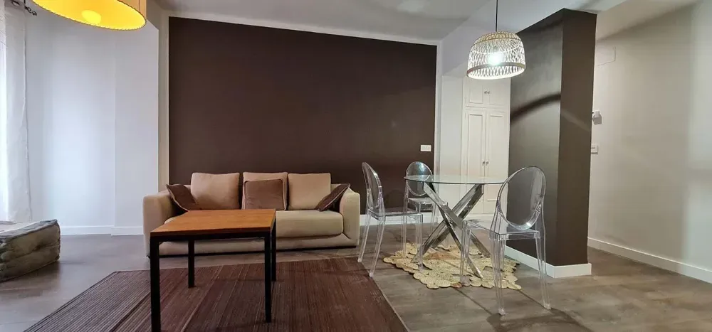 Sala de estar moderna con una pared con acento marrón, un sofá color canela y una mesa de comedor de vidrio.