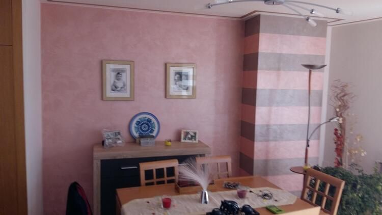 Un comedor con una mesa y sillas y una pared rosa.