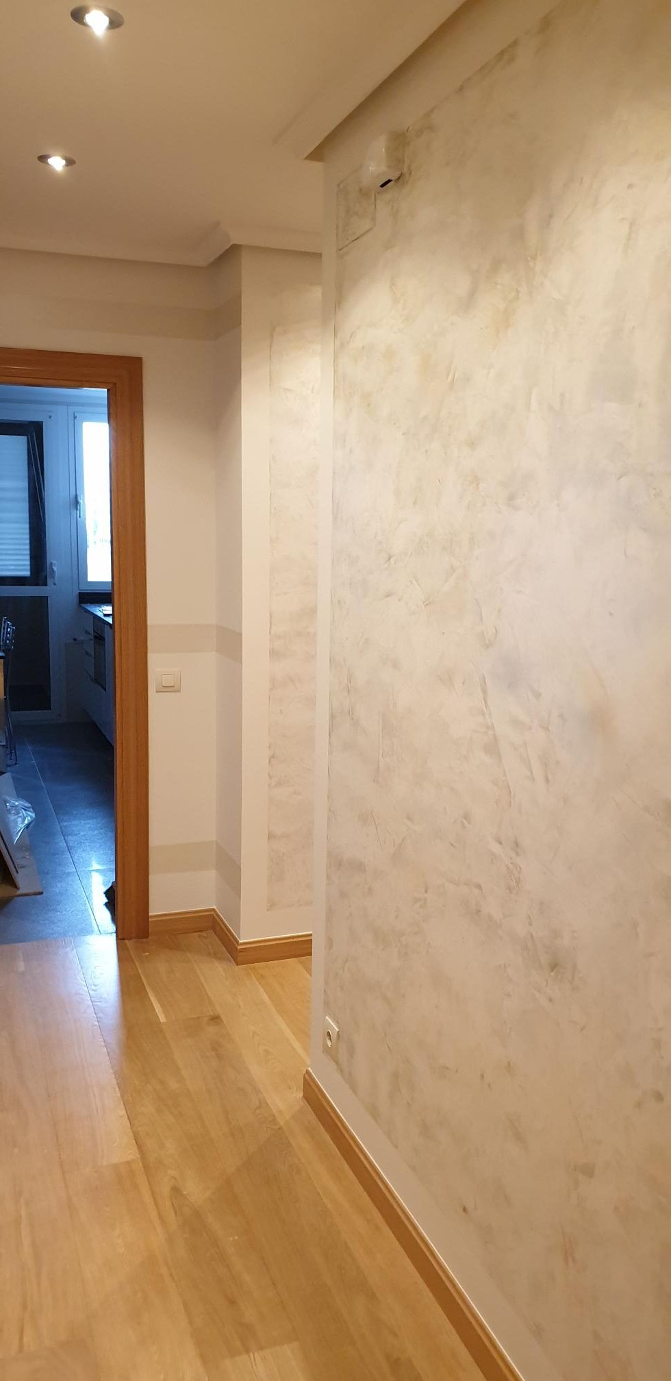 Un pasillo con paredes blancas y suelos de madera que conduce a una cocina.