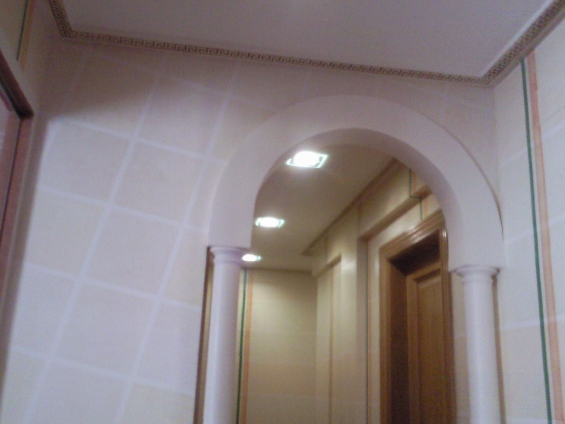 Un pasillo con un arco blanco y una puerta de madera.