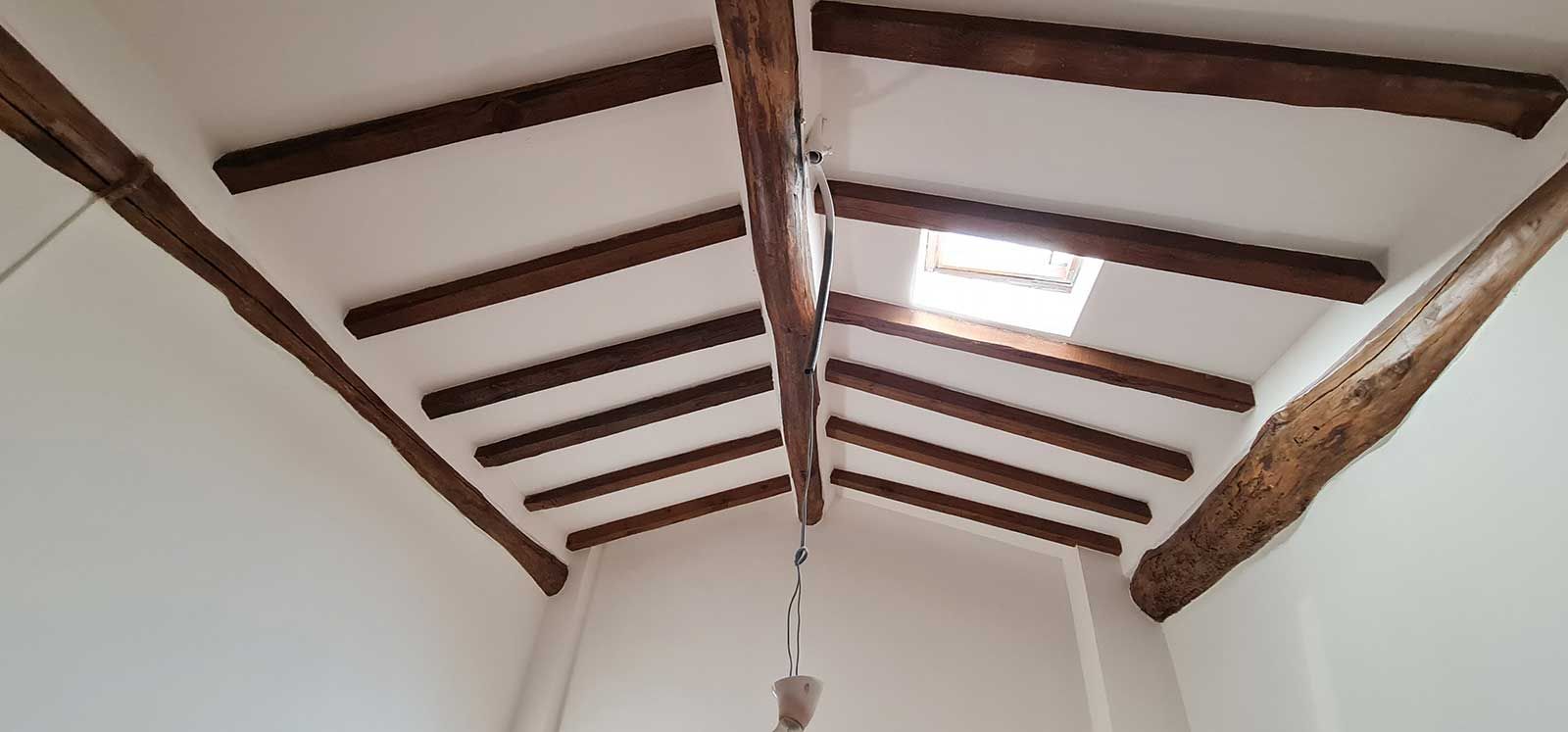 El techo de una habitación con vigas de madera y una ventana.