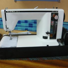 Una máquina de coser Sigma blanca está sobre una mesa de madera.