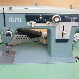 Una máquina de coser Alfamatic está sobre una mesa verde.