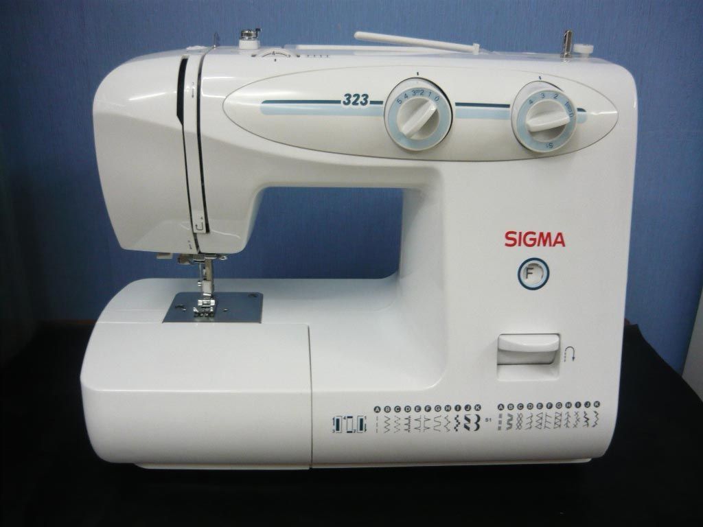 Una máquina de coser Sigma blanca está sobre una mesa.