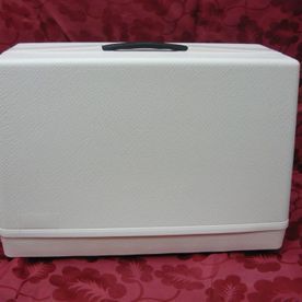 Una caja blanca con un asa negra está sobre una tela roja.