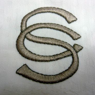 La letra s está bordada sobre una tela blanca.