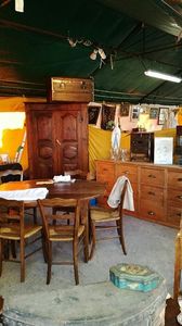 Intérieur d'un entrepôt avec armoire en bois, chaises, commode et petite table sous un toit en toile verte.