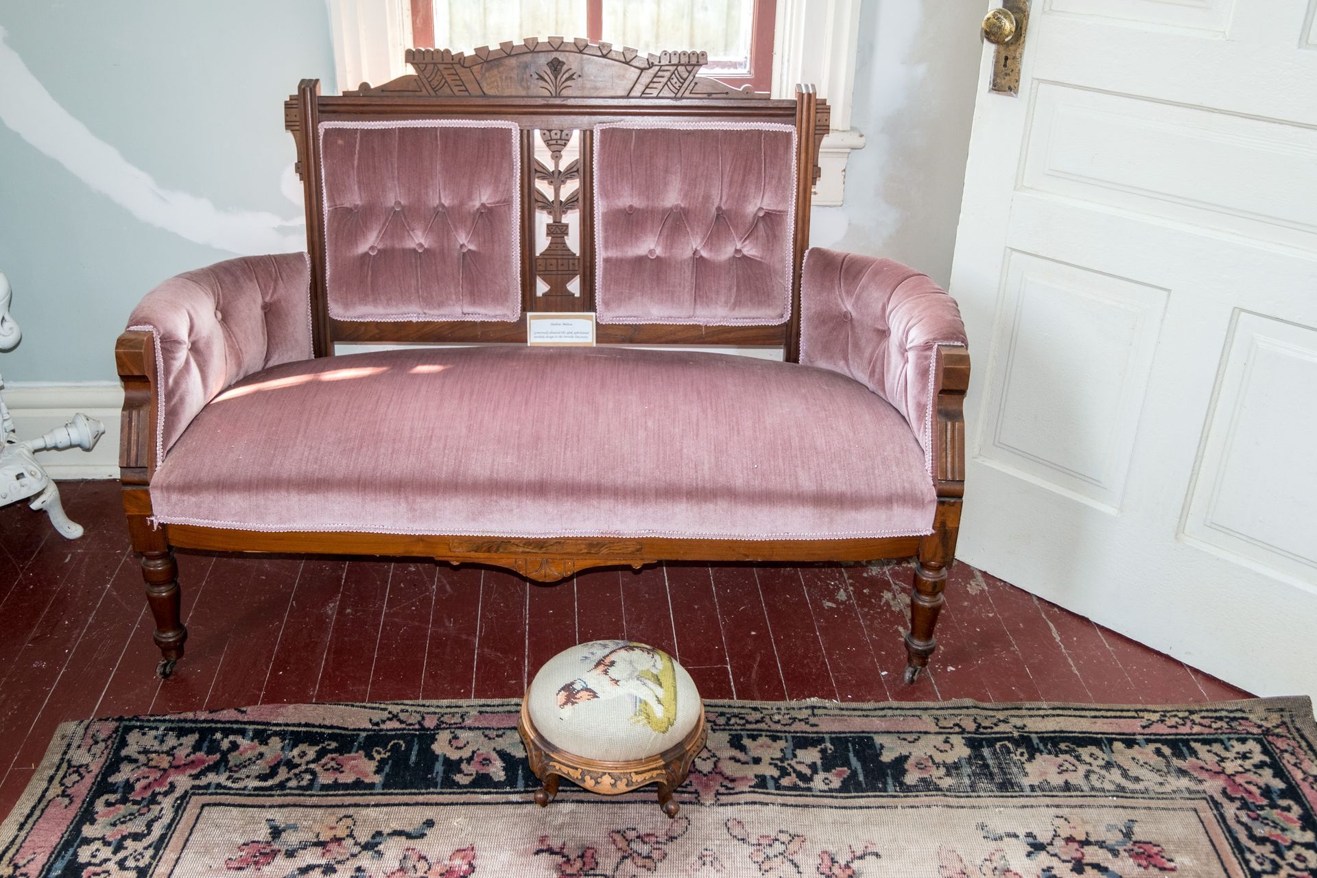 Canapé en velours rose dans une pièce avec un tapis à motifs et un objet en faïence avec pieds dorés posé au sol