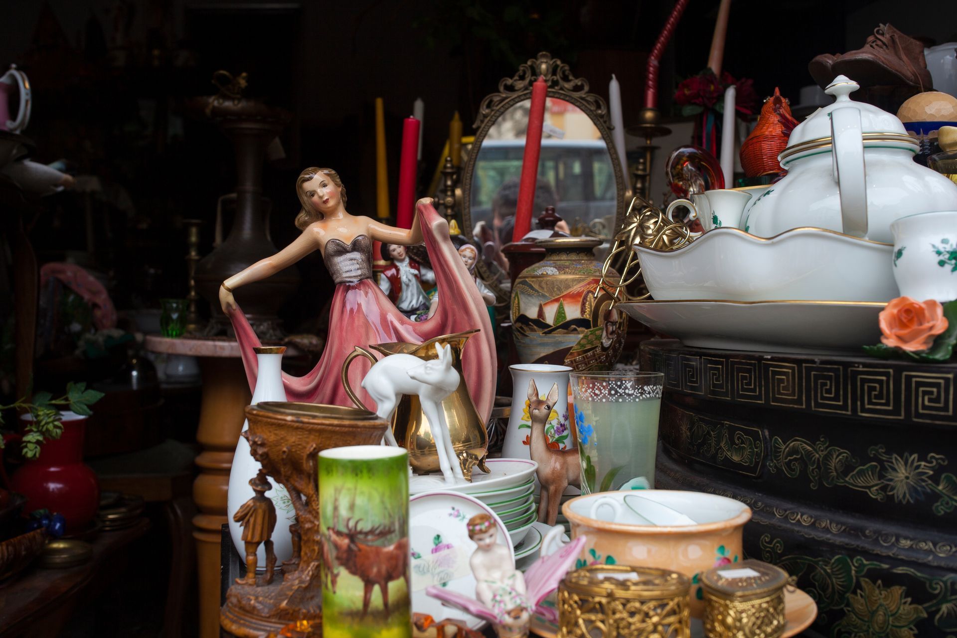 Figurine en robe rose, une théière blanche, des bougies et de nombreux objets décoratifs anciens posés sur une table.