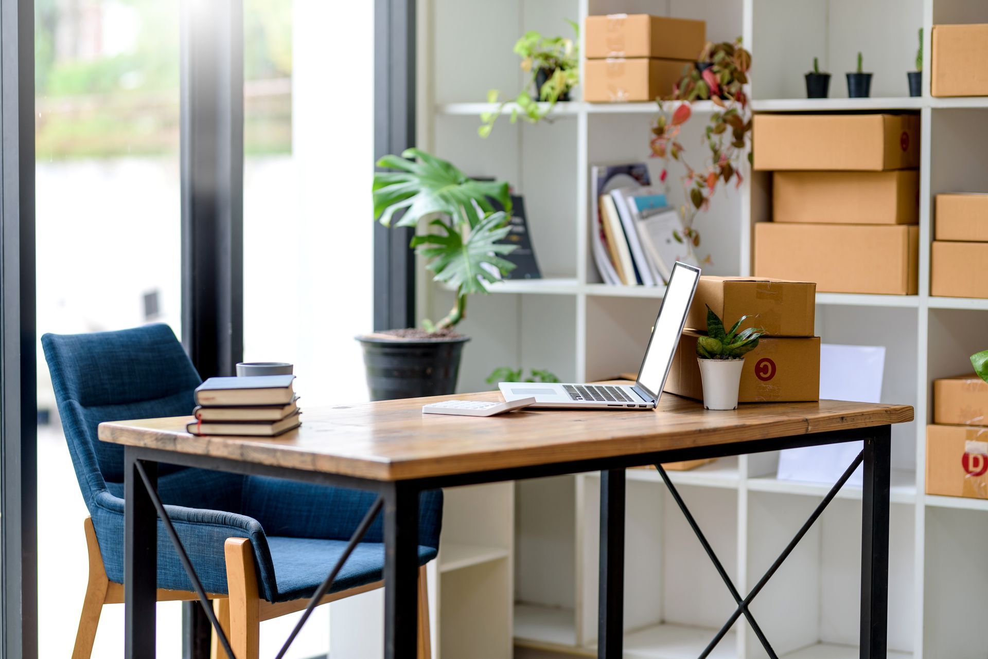 Bureau avec bureau en bois, ordinateur portable, chaise bleue, plantes en pot et étagères blanches