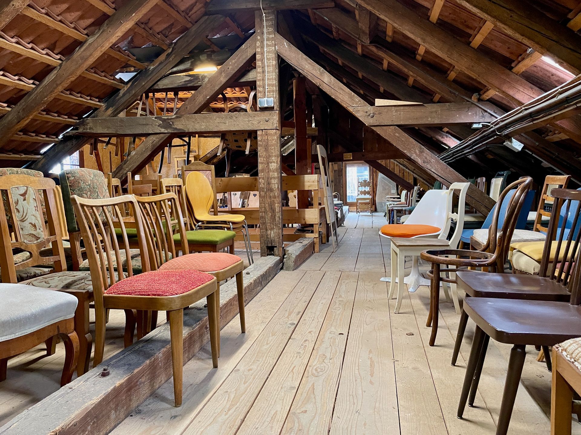 Grenier avec poutres apparentes et rangées de chaises dépareillées sur un plancher en bois