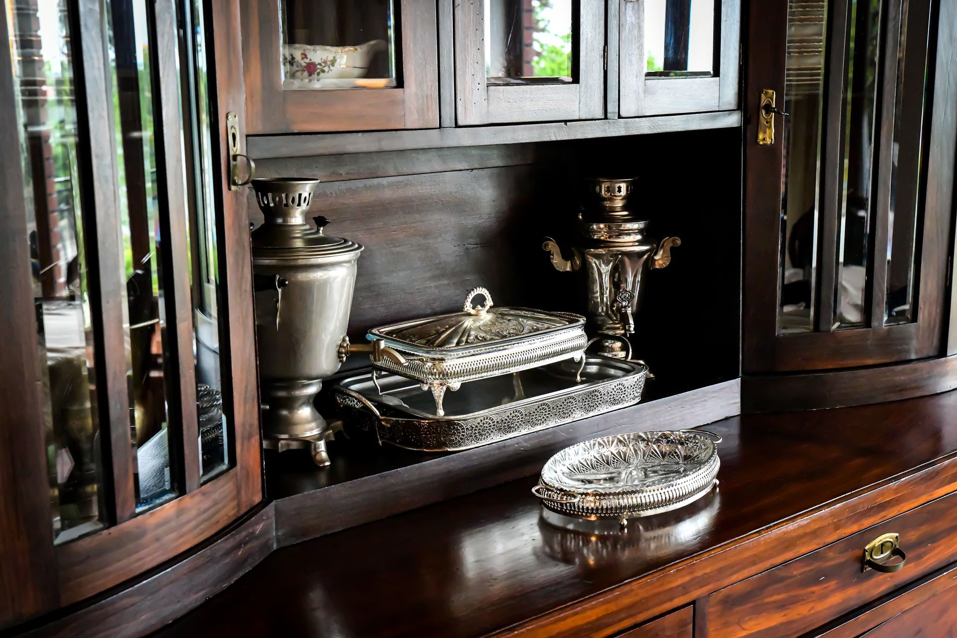 Armoire en bois foncé avec étagères en miroir présentant des objets décoratifs en argent.