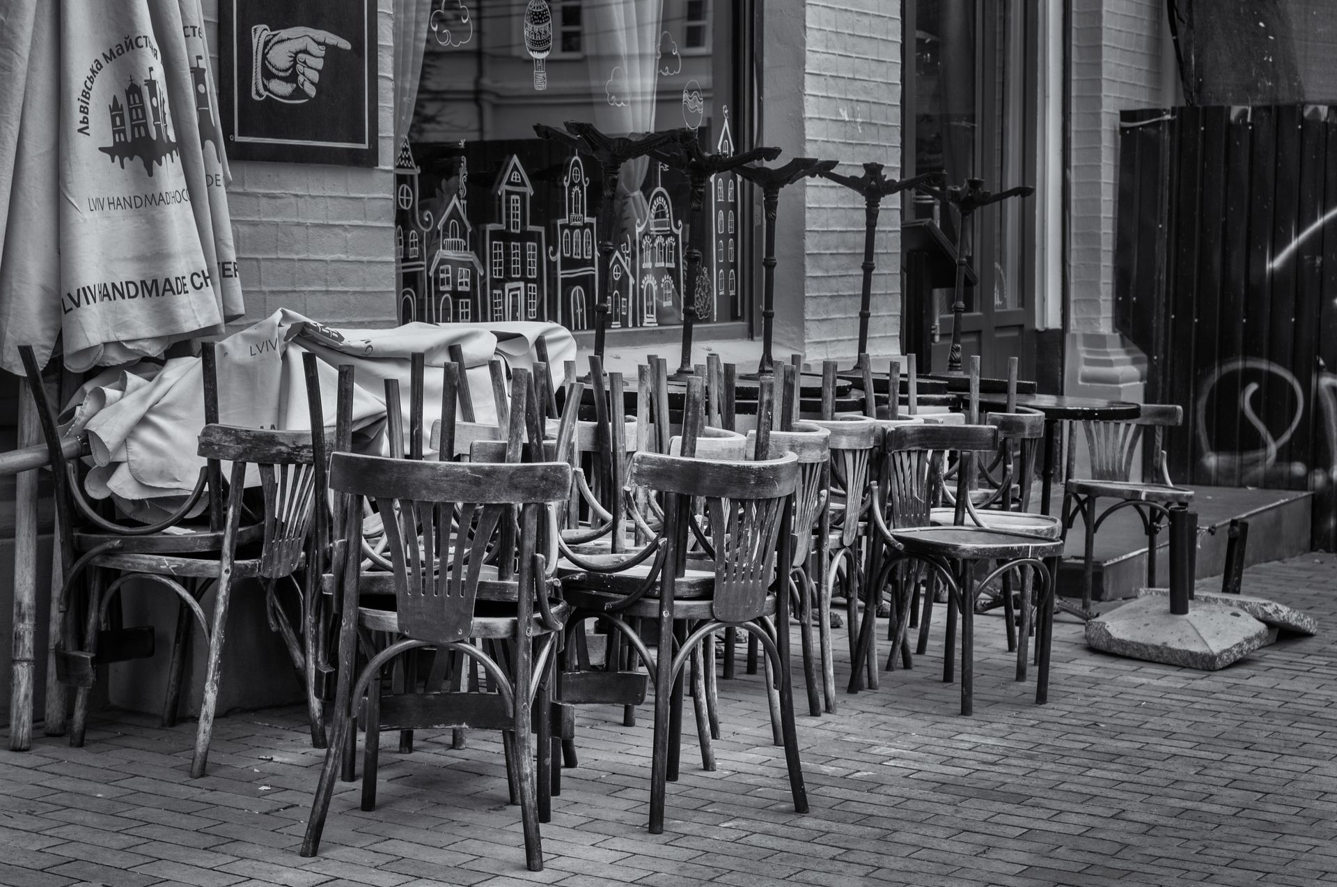 Terrasses de bar avec chaises en bois et tables posées sur un sol pavé, en noir et blanc.