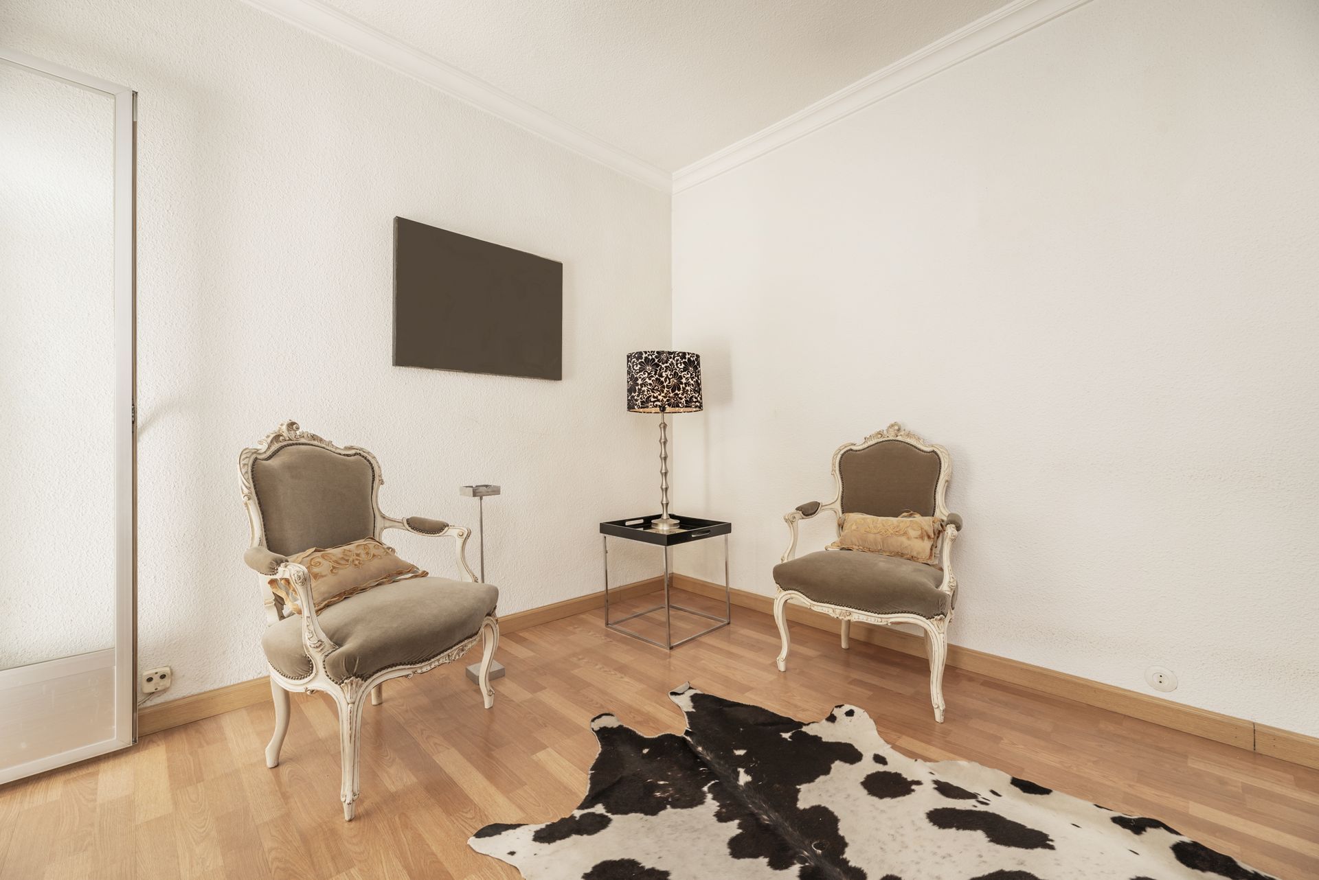Chambre élégante avec deux fauteuils capitonnés, une petite lampe sur une table et un tapis en peau de vache noire et blanche.