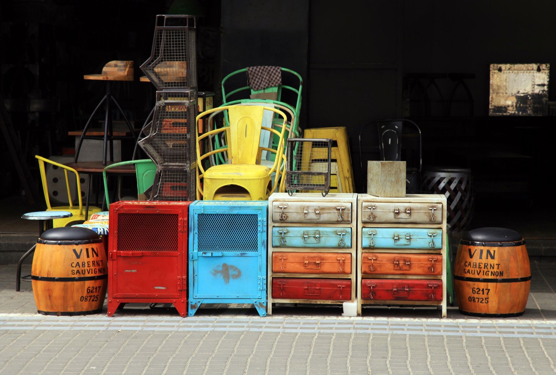Chaises et armoires vintage colorées empilées à côté de tonneaux en bois contre un mur sombre