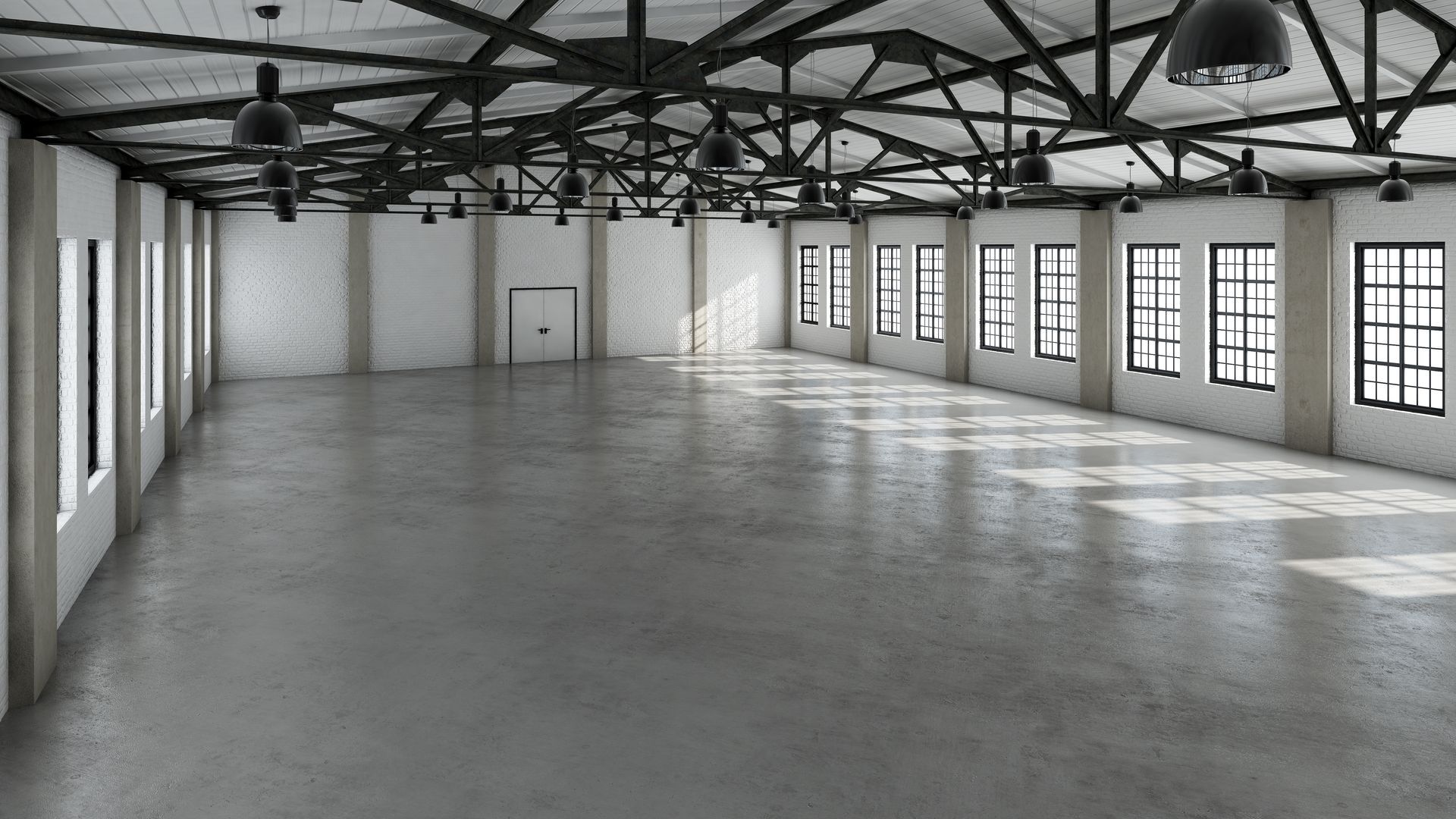 Intérieur d'un entrepôt industriel vide, avec sol en béton, poutres apparentes et une rangée de fenêtres le long des murs.