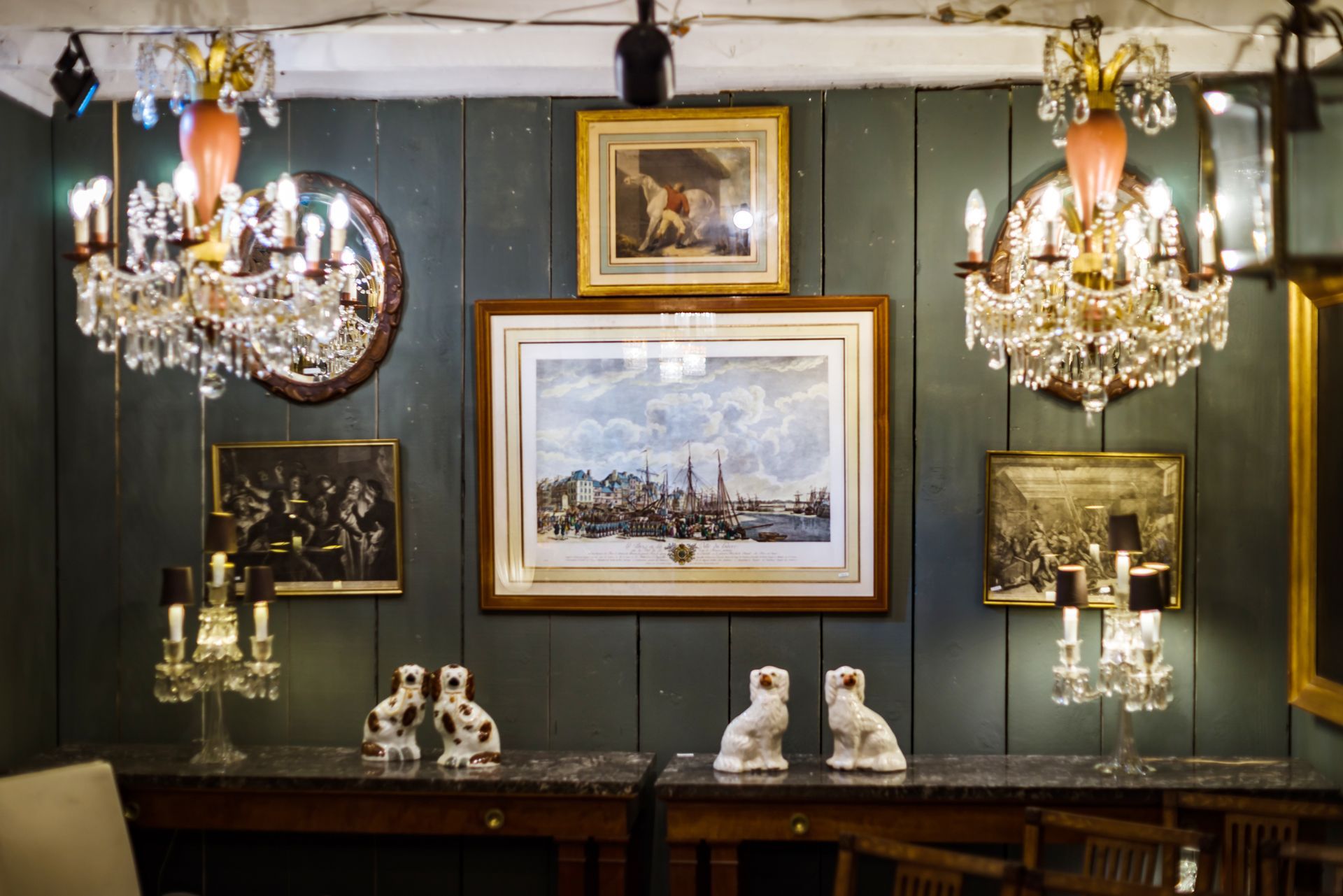 Pièce ancienne avec des murs en lambris verts, des lustres, des tableaux, des bibelots et une table en bois foncé