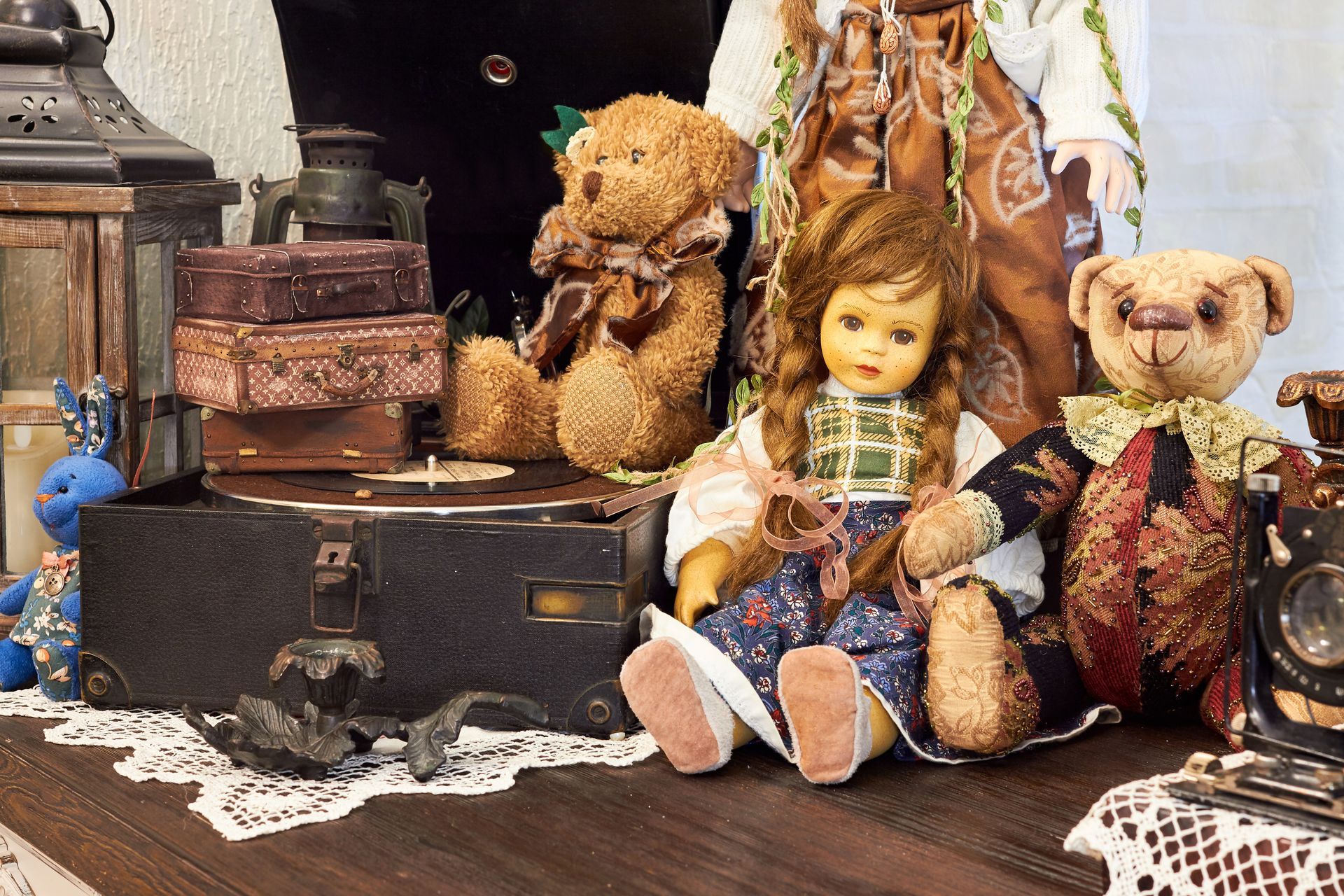Des ours en peluche et des poupées vintage sont assis à côté de valises anciennes empilées sur une table en bois