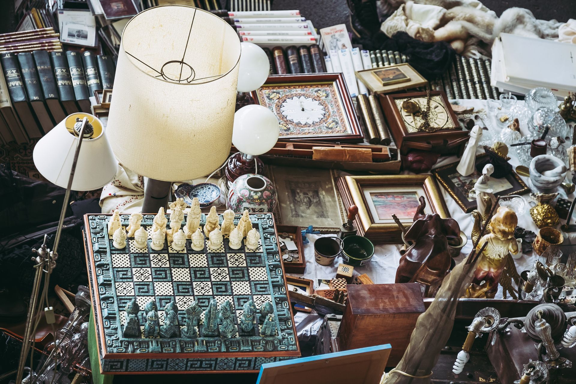 Un étal de marché d'antiquités bondé, proposant lampes, tableaux encadrés, livres et objets vintage divers.
