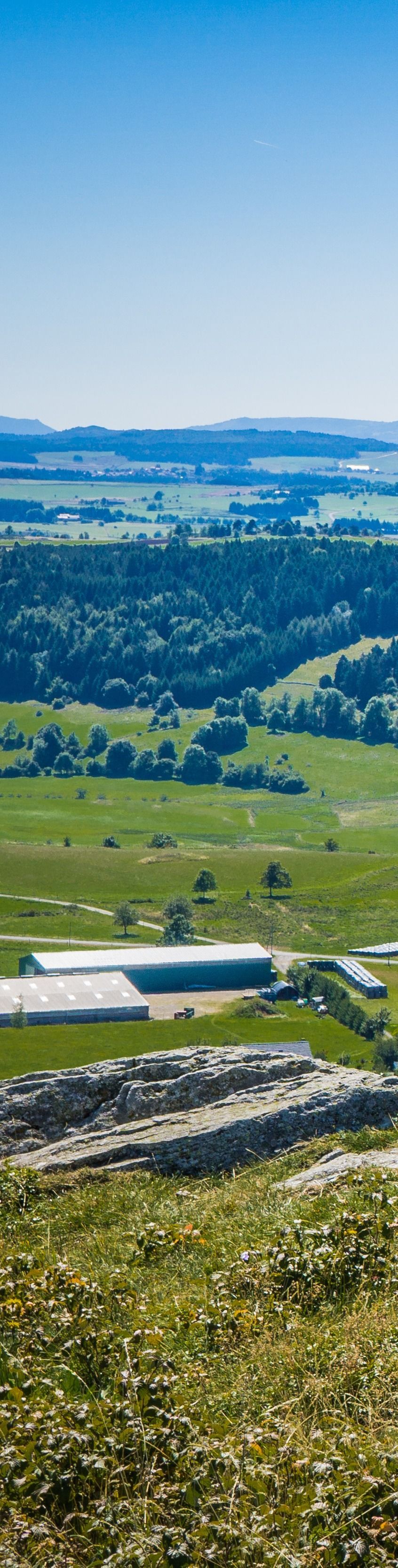 Vaste vallée verdoyante traversée par une rivière, collines bleues au loin et ciel nuageux