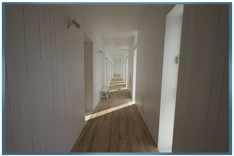 Long couloir lumineux avec parquet, murs blancs et lumière naturelle.