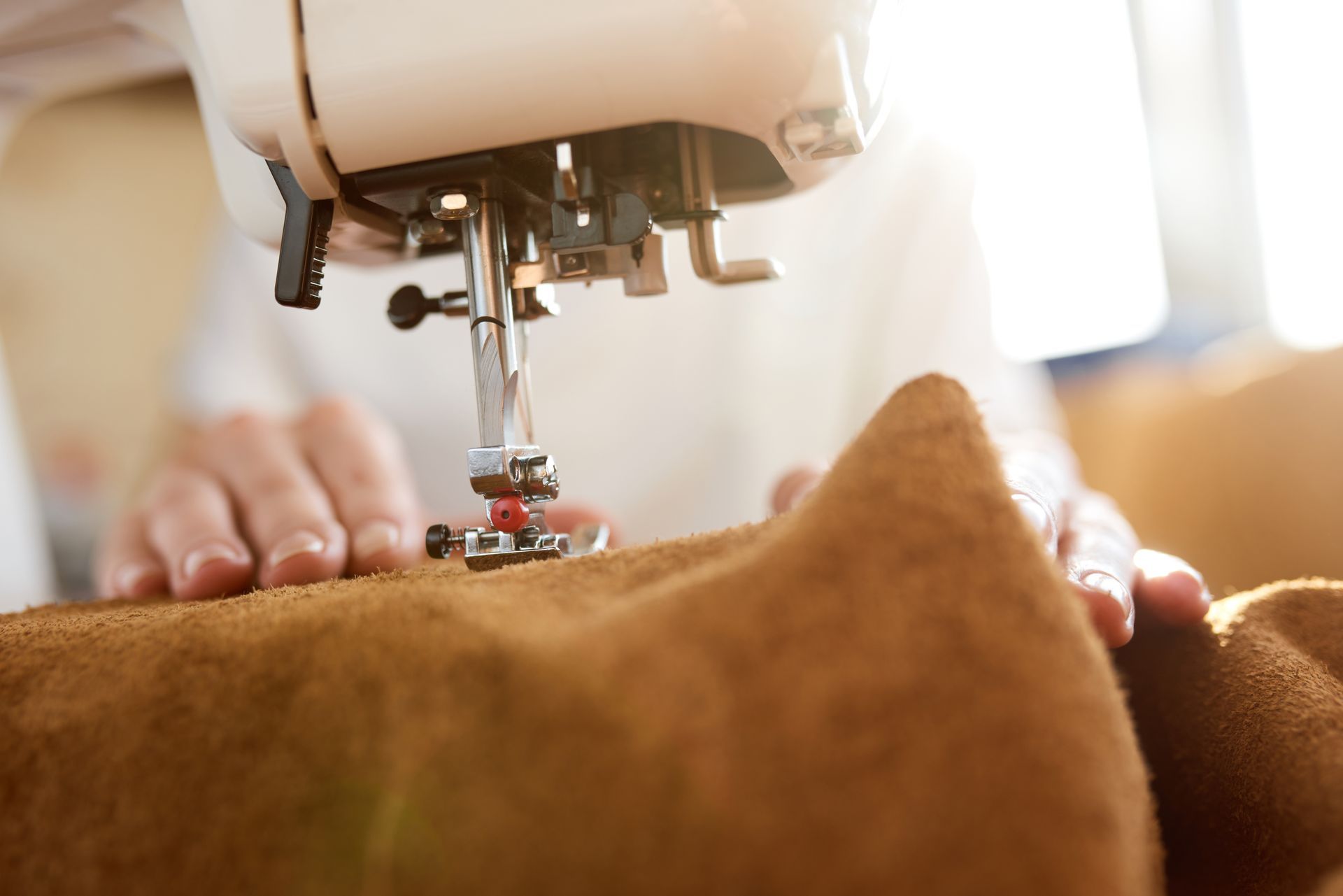 Gros plan sur des mains qui cousent un tissu marron à la machine à coudre