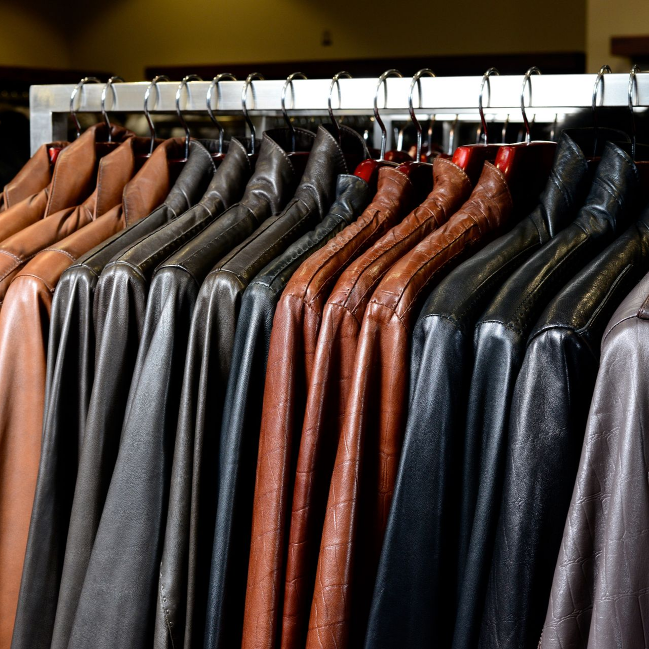 Rangée de vestes en cuir sur des cintres dans un magasin de vêtements, dans des tons noirs, bruns et gris