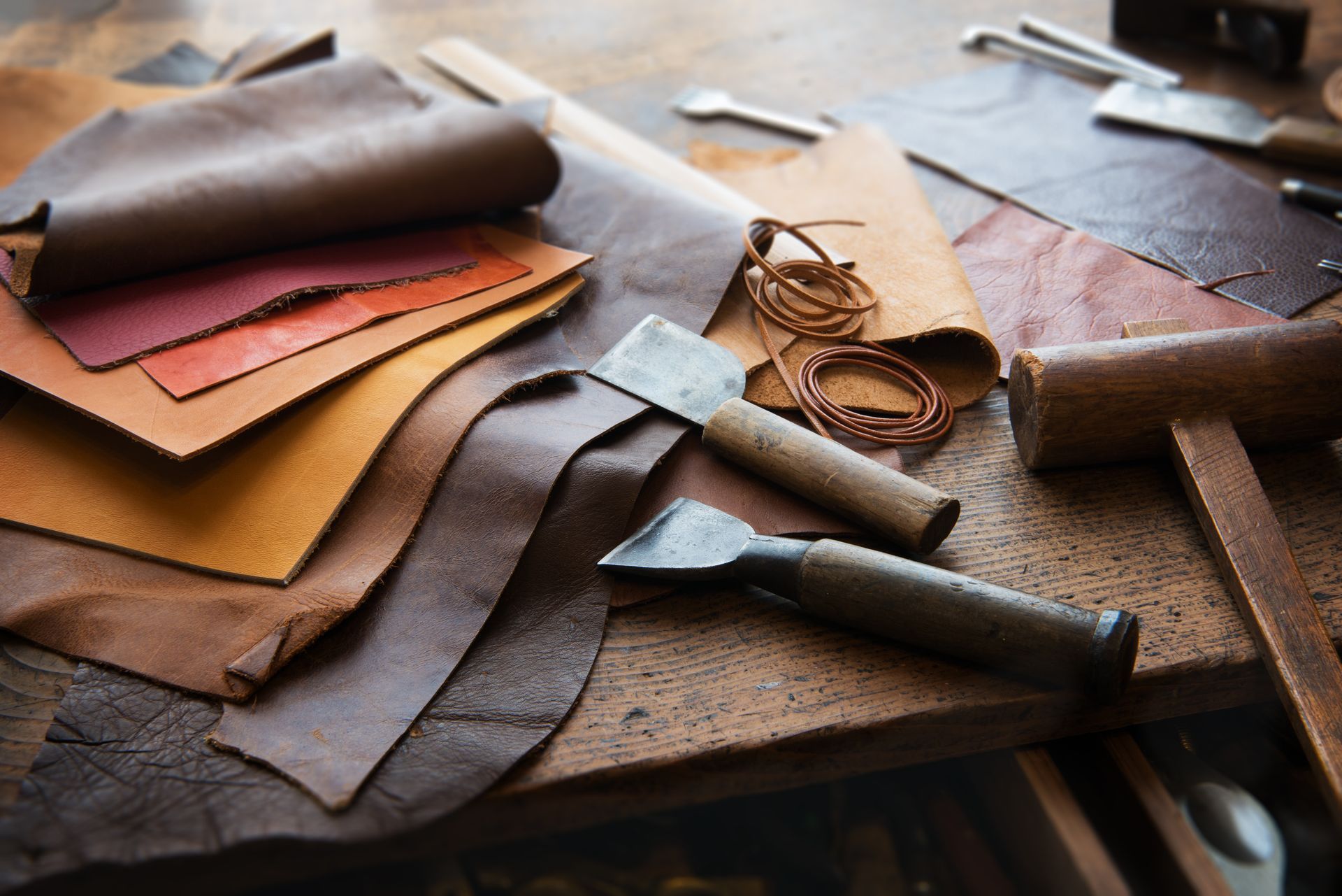 Des outils de maroquinerie et des pièces de cuir colorées sont disposés sur un établi en bois.