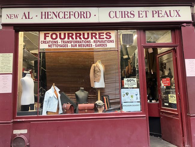 Devanture bordeaux avec des manteaux de fourrure et des peaux exposés en vitrine, et une enseigne indiquant Fourrures