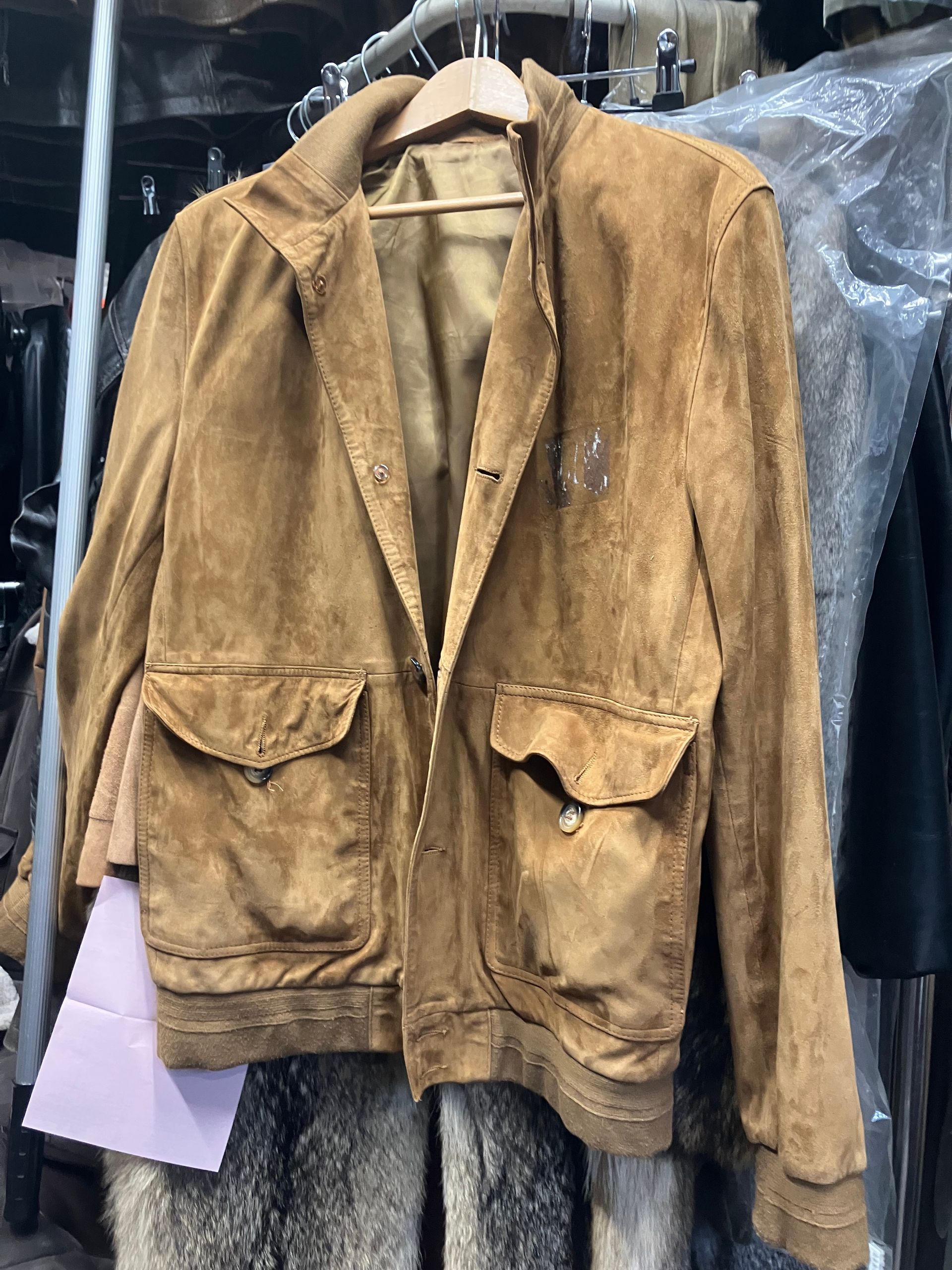Veste en daim marron suspendue à un portant, avec de grandes poches plaquées à l’avant et des marques d’usure visibles.