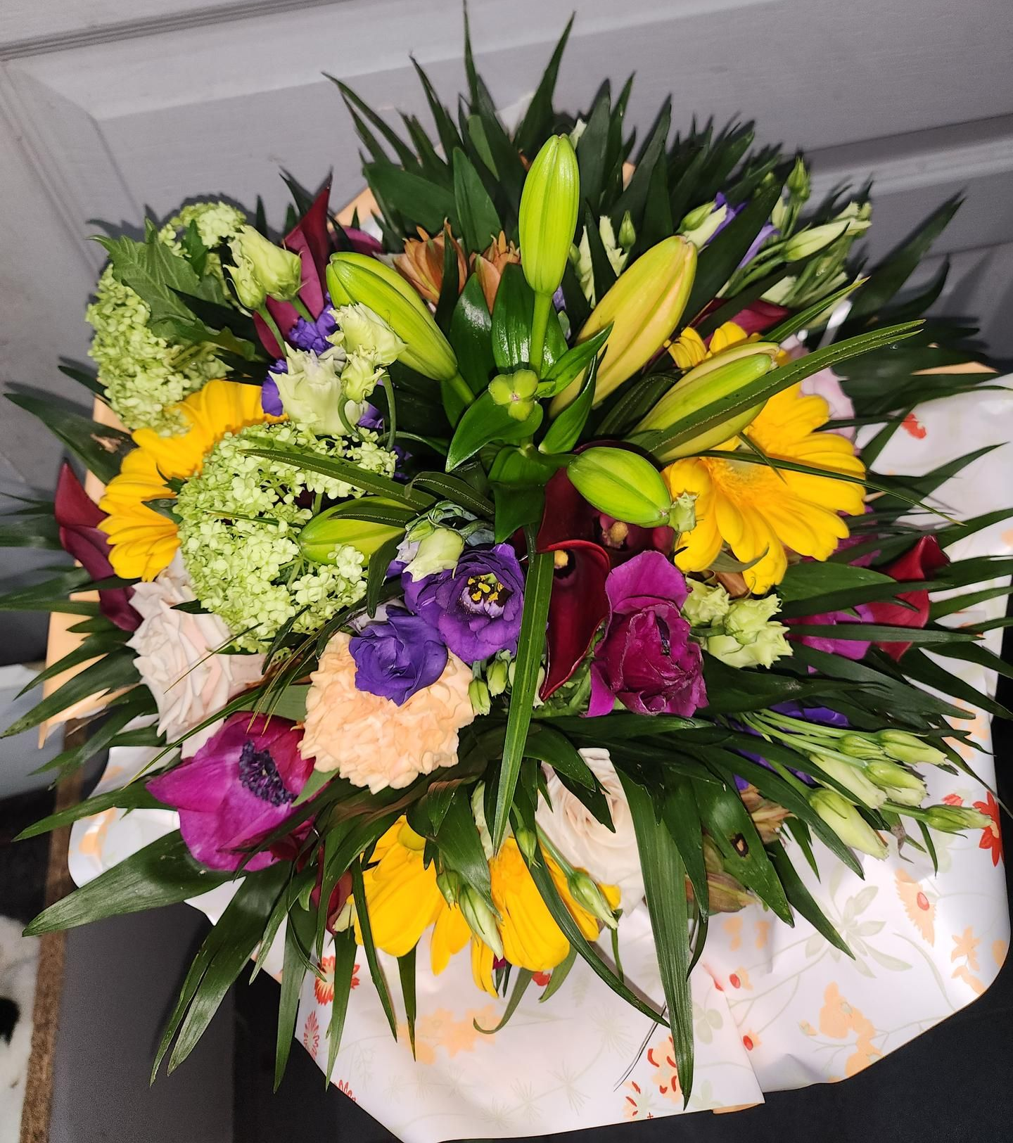 Bouquet de fleurs colorées, comprenant des gerberas jaunes, des lys et des fleurs violettes.