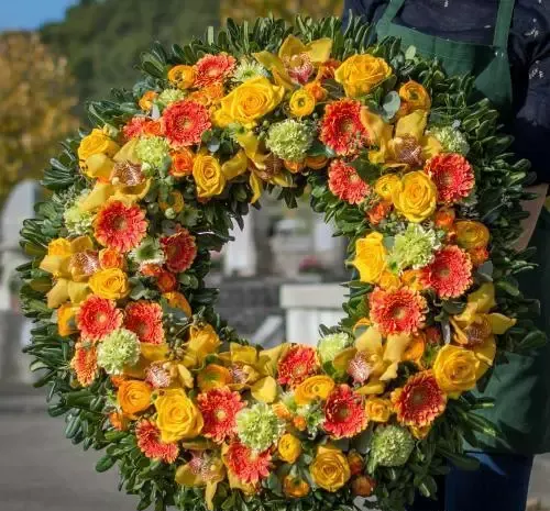Couronne florale avec des fleurs jaunes et oranges, tenue par une personne dans un tablier vert.