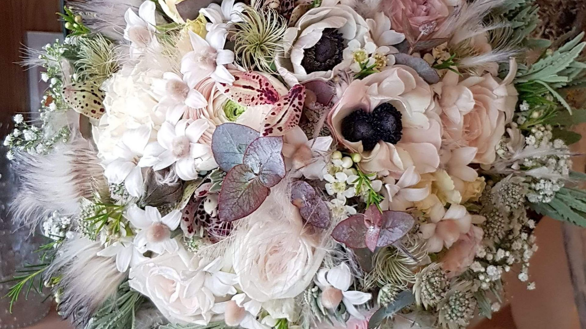 Gros plan d'un bouquet de mariée aux tons neutres avec des roses, des plumes et divers feuillages.