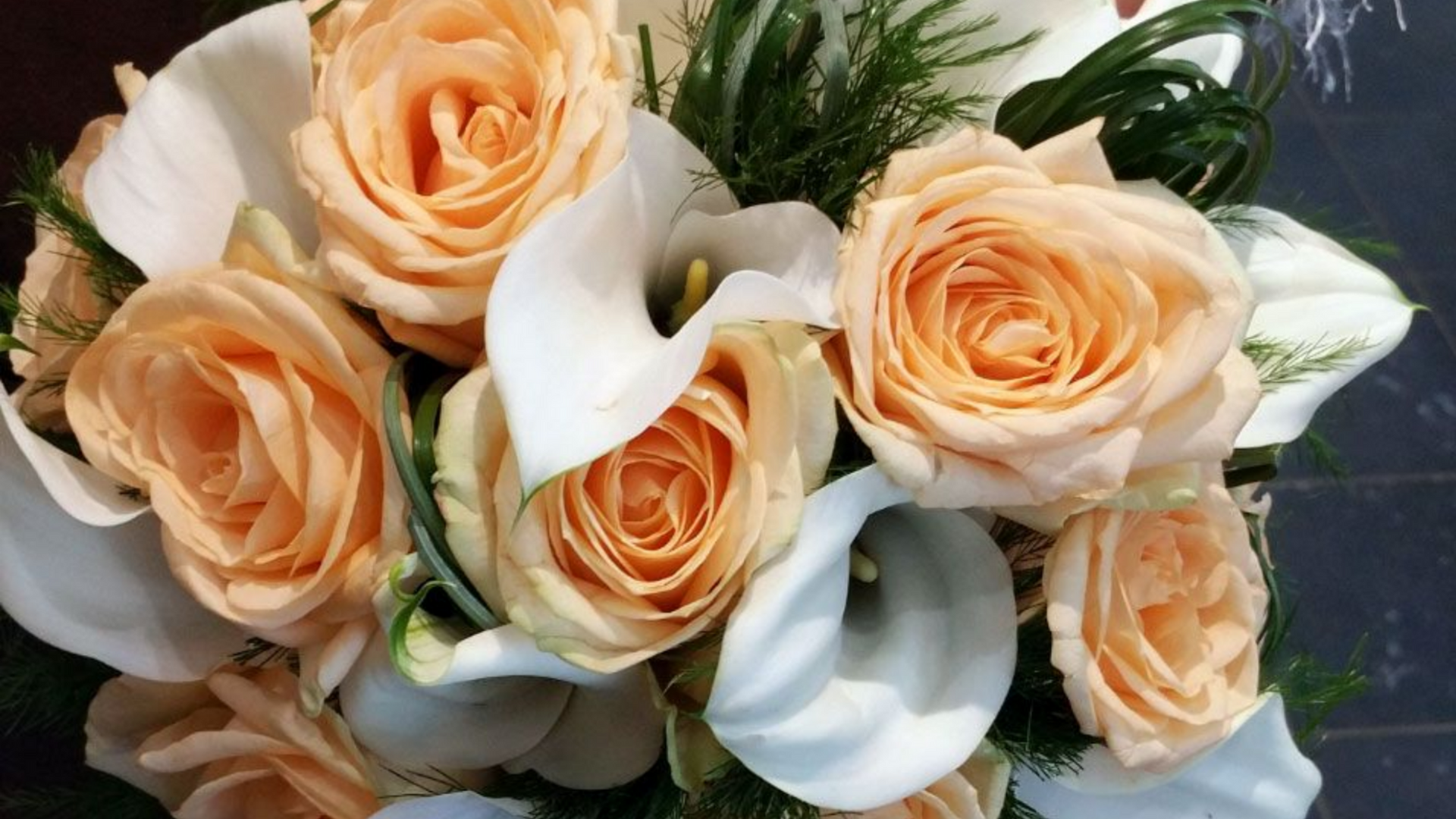 Roses pêche et lys calla blancs dans une composition florale.