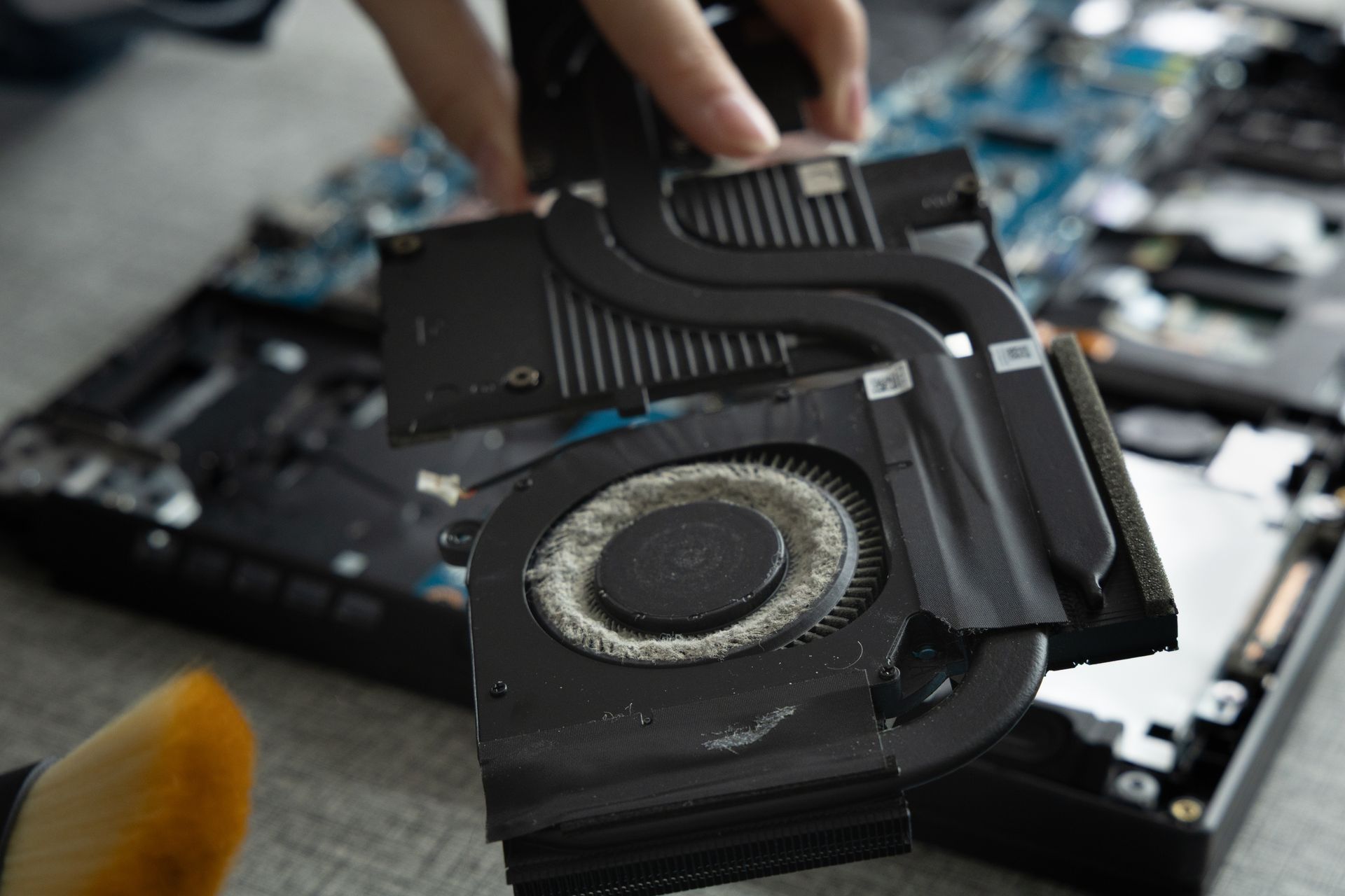 Démontage du bloc ventilateur de refroidissement d'un ordinateur portable. Dissipateur thermique, ventilateur et tubes en métal noir présentant de la poussière visible.