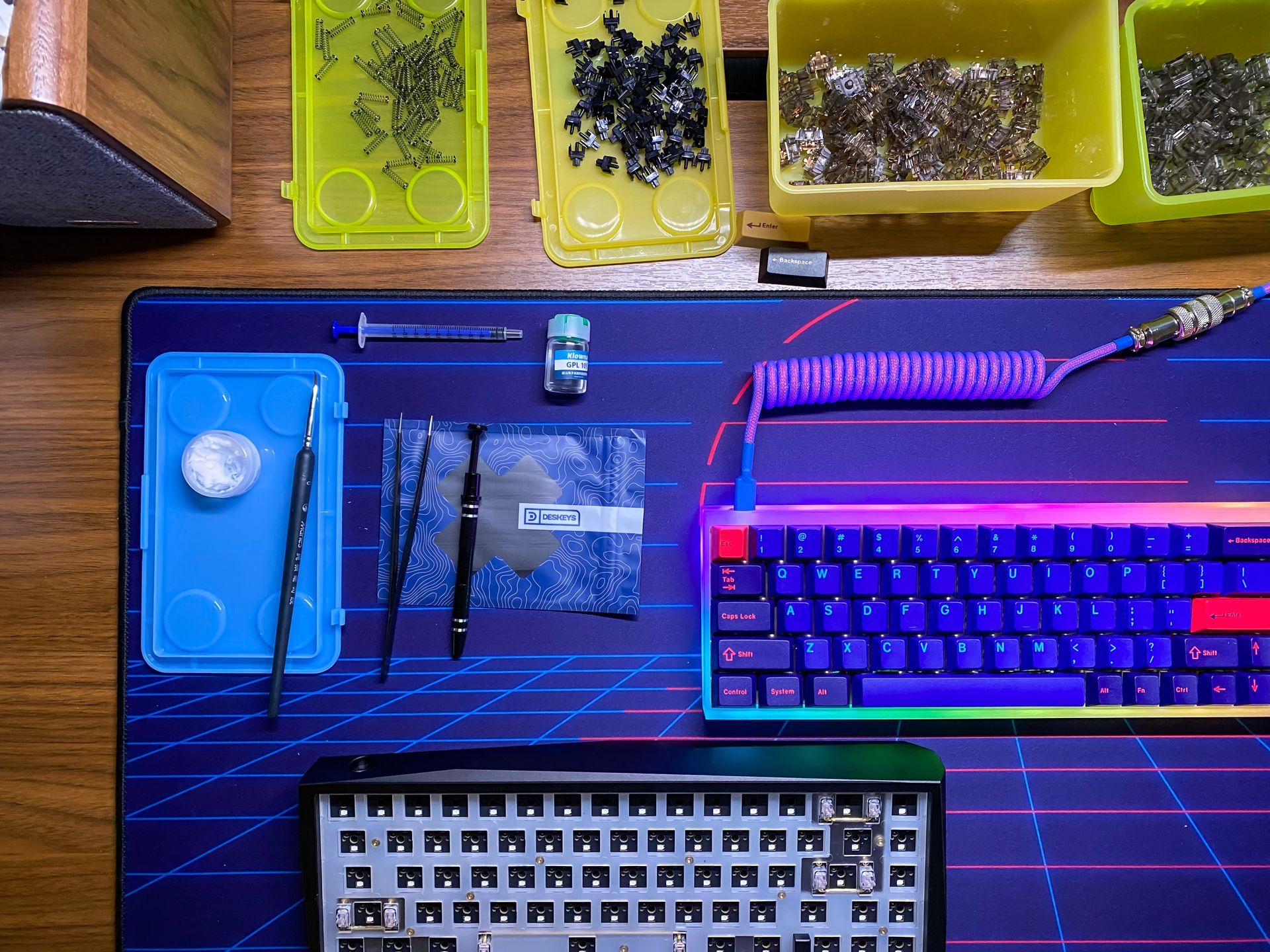 Configuration d'un clavier mécanique à monter soi-même. Clavier, composants dans des plateaux, outils et câble enroulé sur un tapis de bureau.