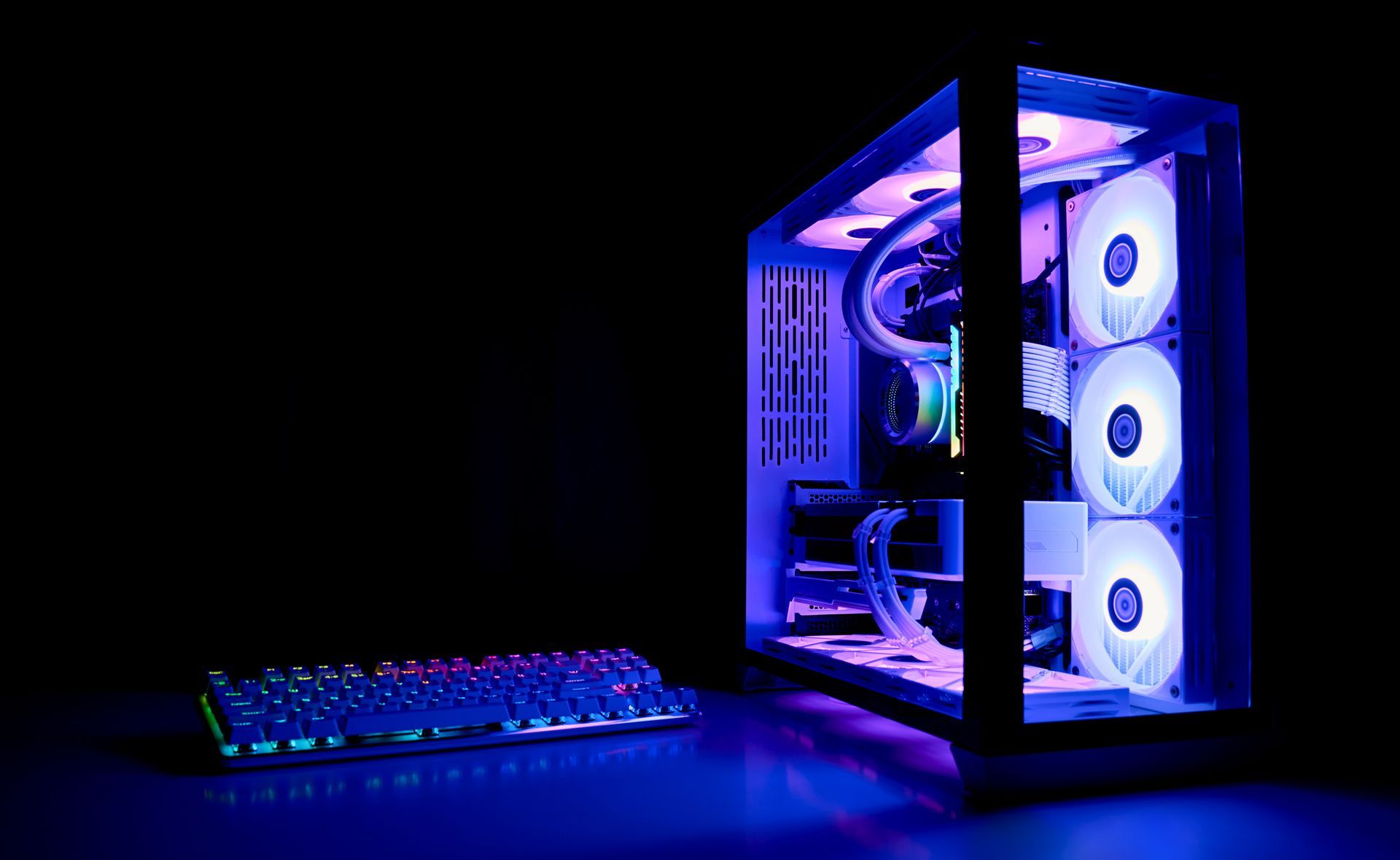 Ordinateur de bureau illuminé, avec trois ventilateurs et un clavier, brillant de bleu et de violet dans un environnement sombre.