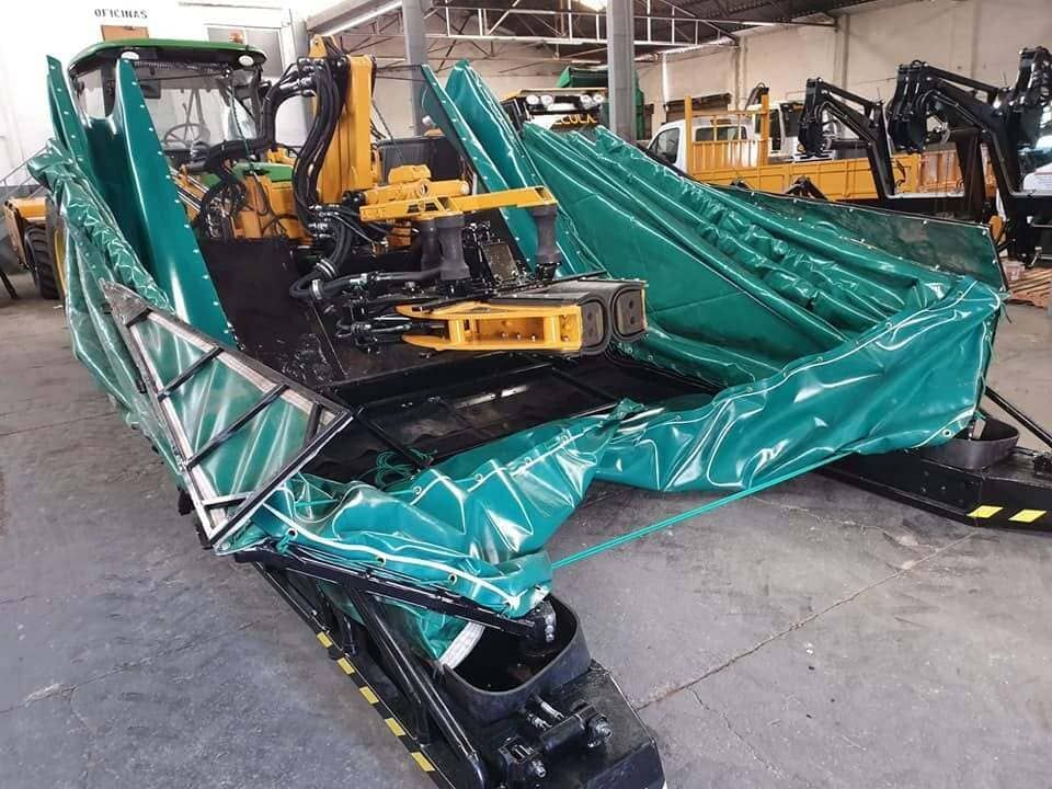 Lonas verdes cubren maquinaria industrial en un almacén, junto con equipos amarillos y una estructura metálica.