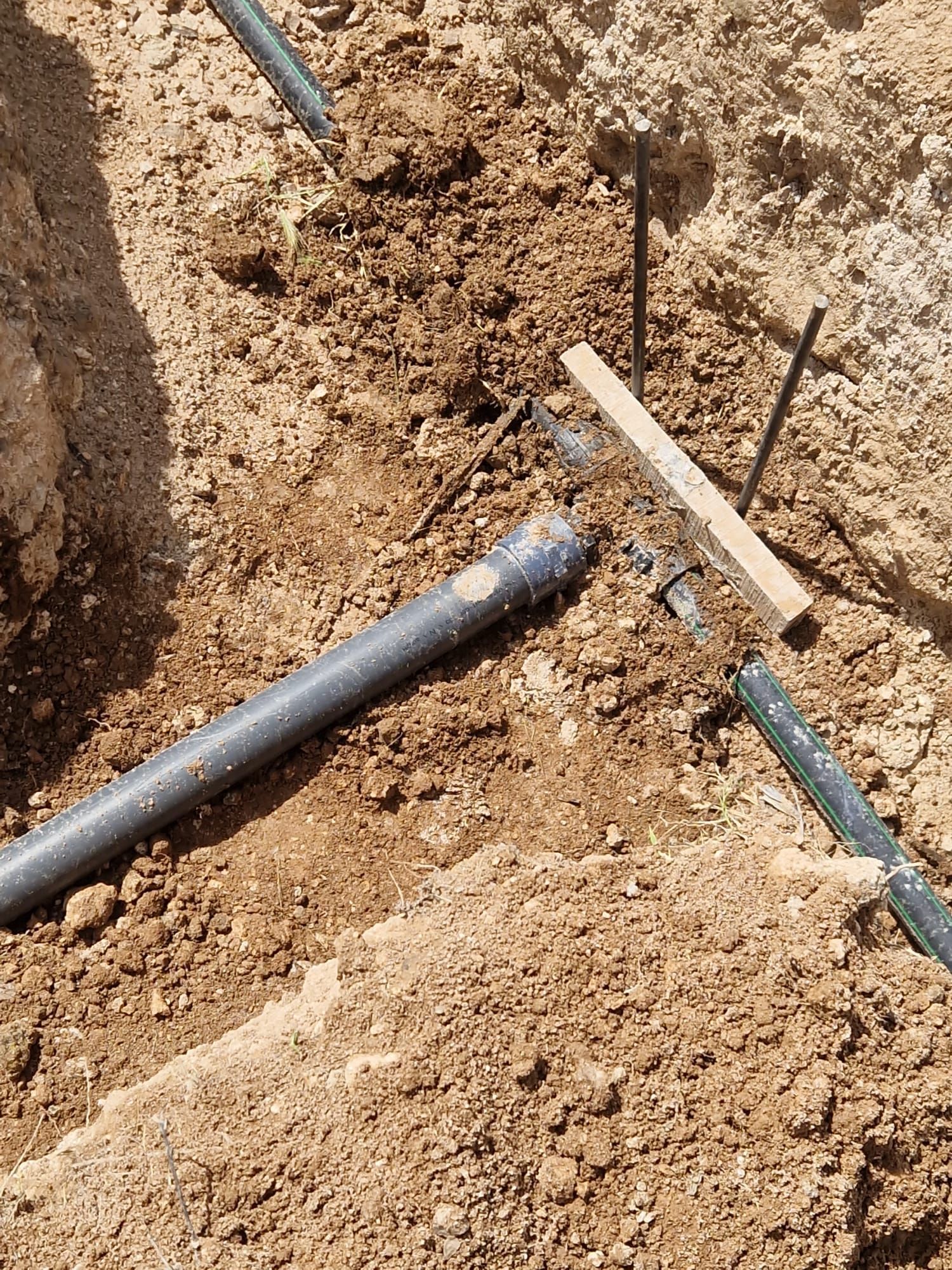 Tubería negra y zanja expuestas en suelo seco durante la excavación, con herramientas cerca