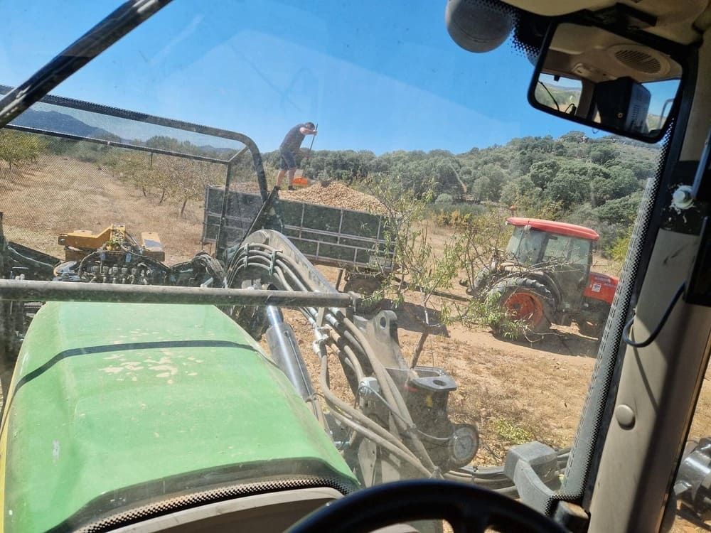 Vista desde la cabina de un tractor sobre un campo, con otro tractor y una persona trabajando al fondo.