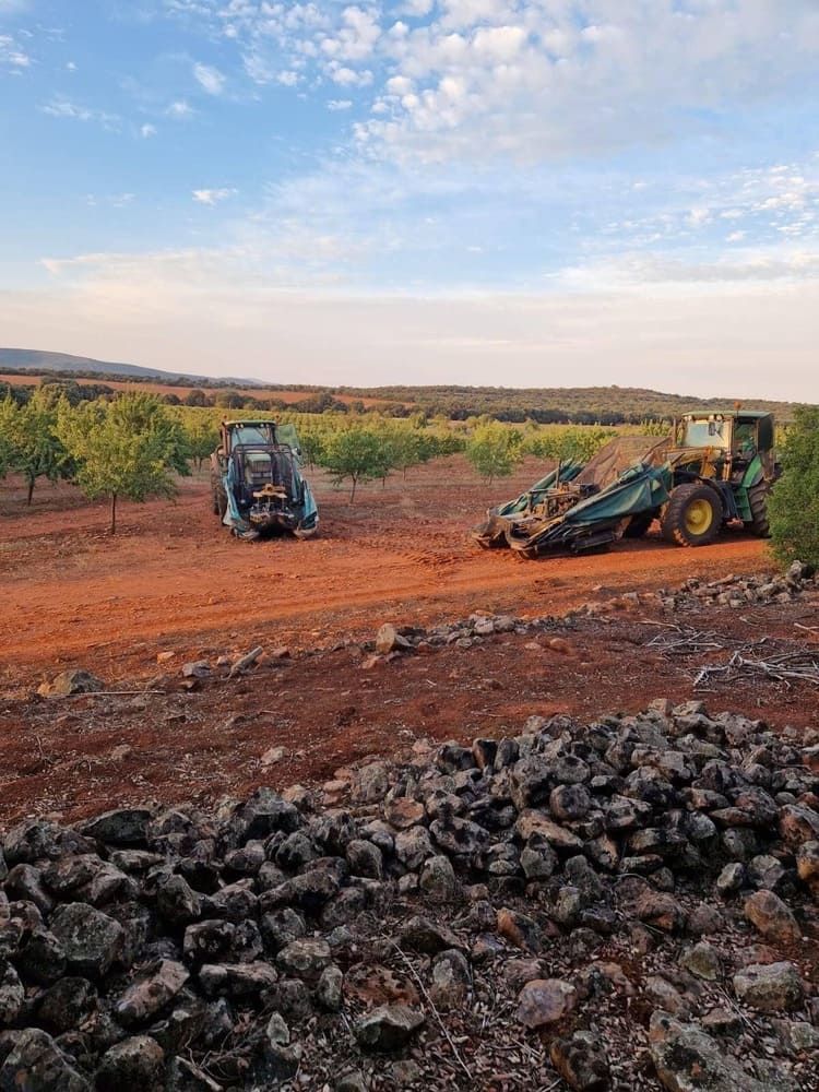 Dos tractores en un campo de tierra rojiza bajo un cielo parcialmente nublado, con rocas oscuras en primer plano