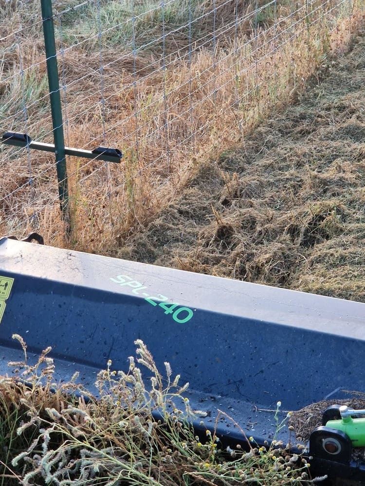 Primer plano de un apero agrícola azul verdoso con maleza al lado de una cerca de alambre en una pradera seca