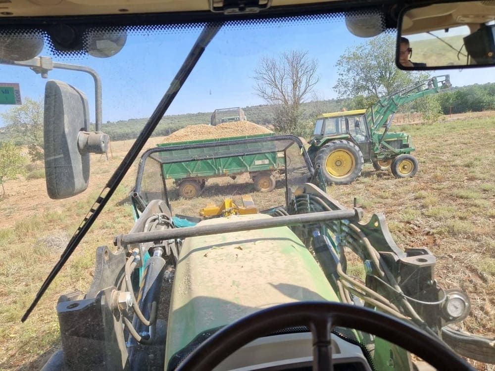 Vista desde la cabina de un tractor de un campo polvoriento y otro tractor delante, bajo un cielo despejado