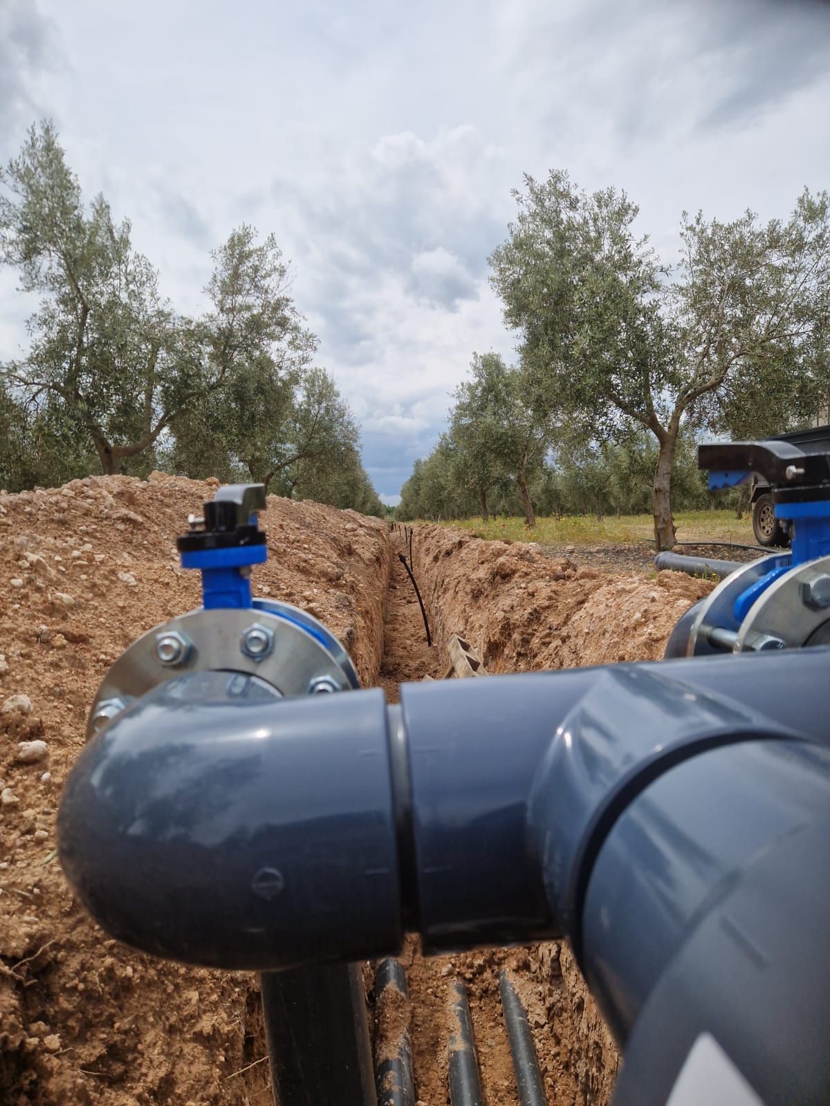 Válvulas azules en una zanja de una obra, con árboles y un cielo nublado al fondo