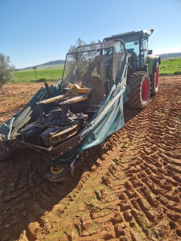Tractor volcado con la pala cargadora delantera dañada en un campo embarrado bajo un cielo azul despejado