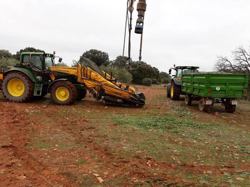 Tractores verdes y una máquina agrícola amarilla en un campo embarrado bajo un cielo nublado