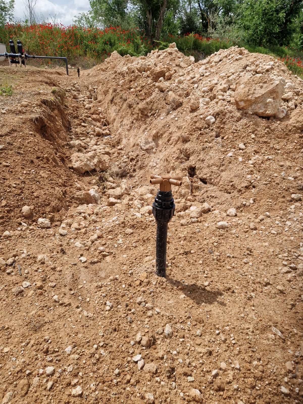 Una zanja estrecha de tierra junto a un gran montón de tierra excavada en una zona de obras al aire libre.