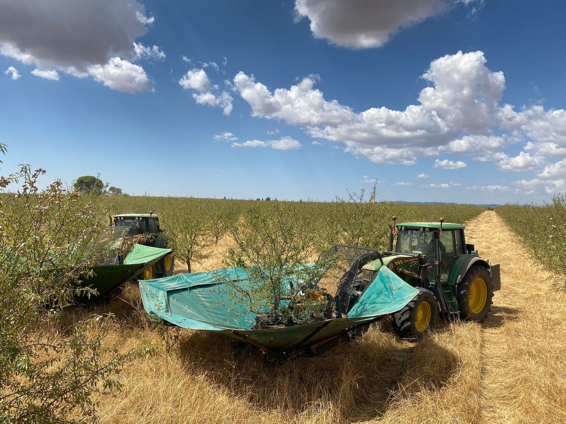 Dos tractores en un campo, remolcando un amplio apero agrícola verde bajo un cielo nublado.